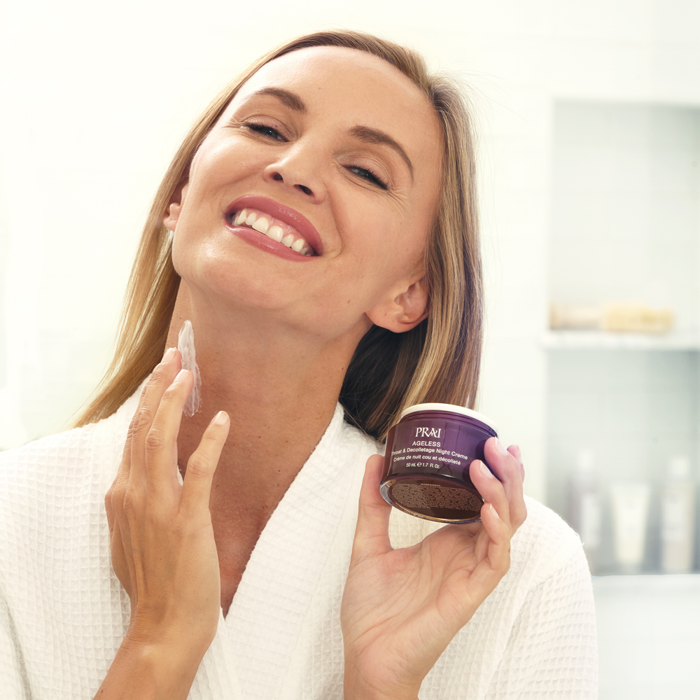 A woman applying PRAI Ageless Throat & Decolletage Night Creme