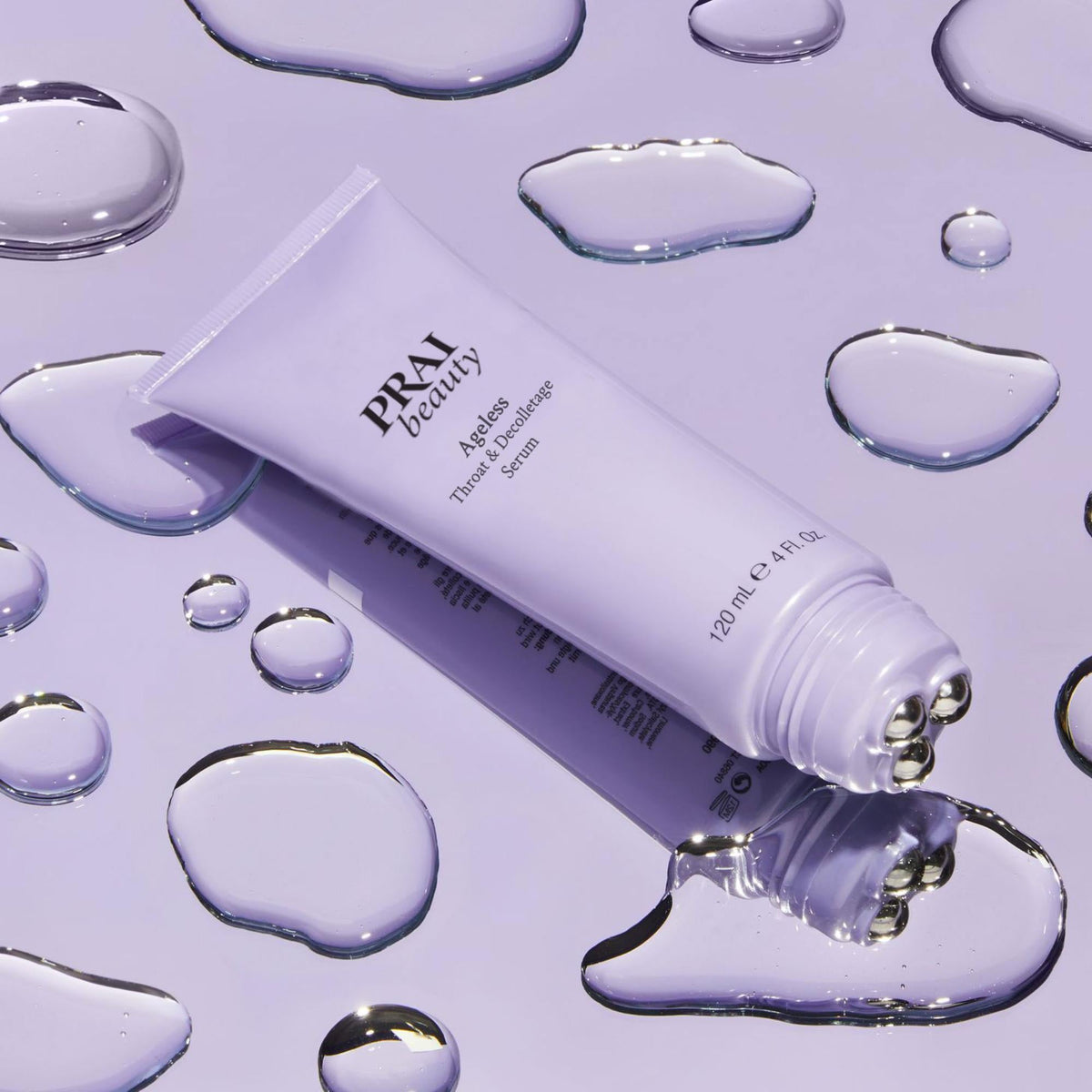 PRAI Beauty Ageless Throat & Decolletage Serum, tube with roller tip on a lilac surface with water droplets