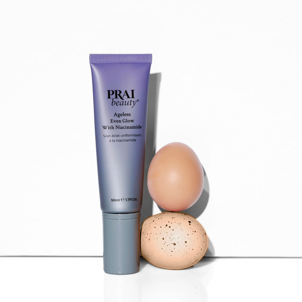 PRAI Beauty Ageless Even Glow with Niacinamide, tube standing beside smooth stones on white
