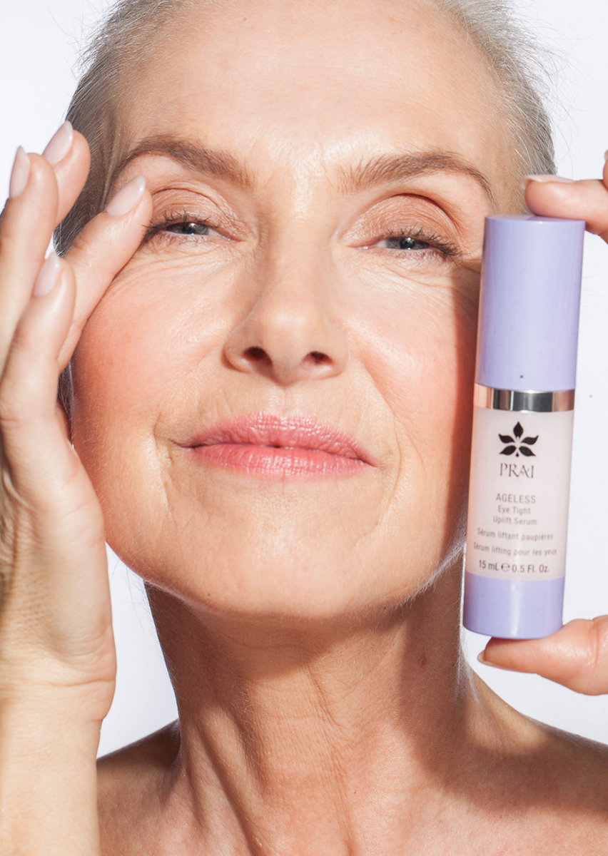PRAI Beauty Ageless Eye Tight Uplift Serum, woman holding the bottle beside her eye