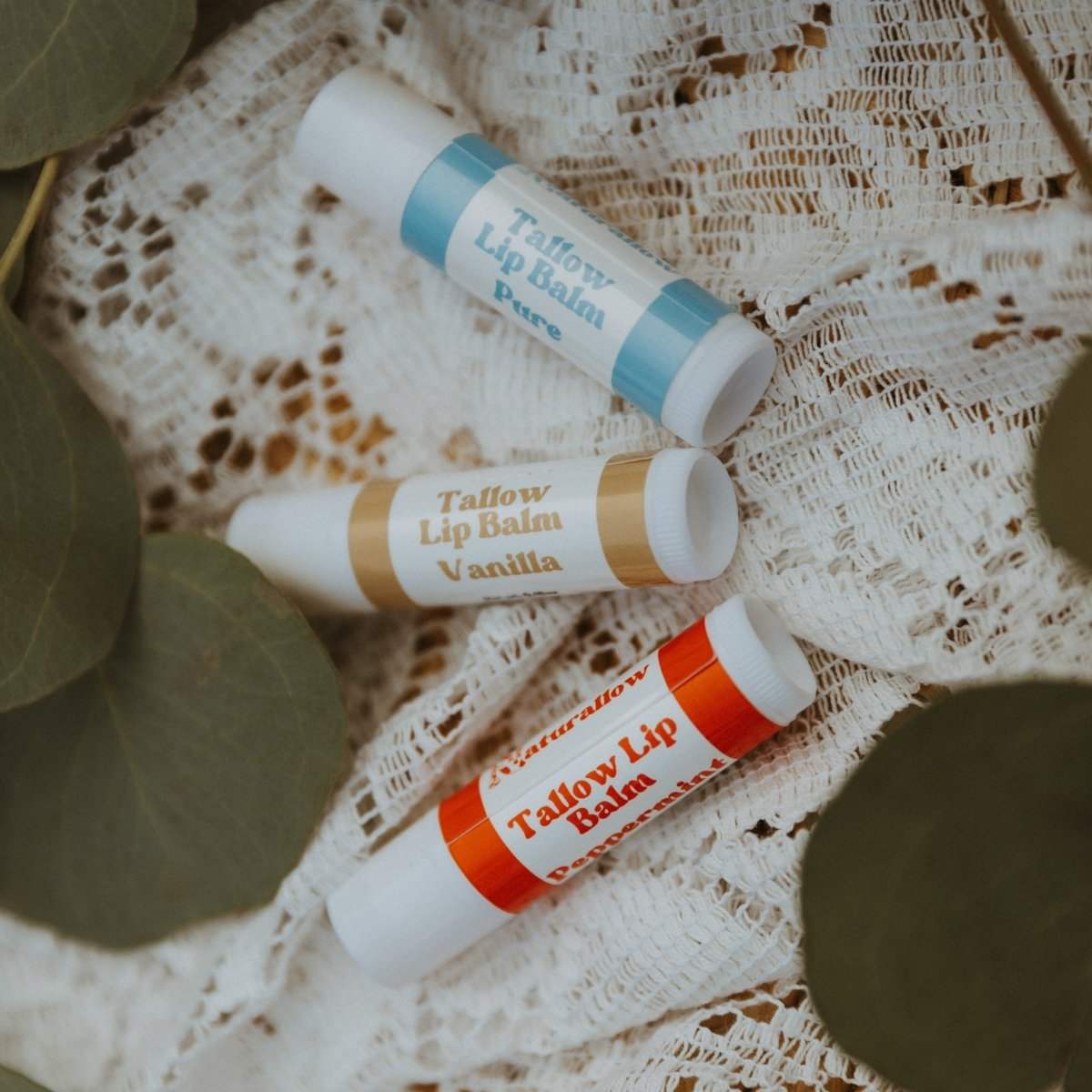 Naturallow Tallow Lip Balm, Pure, Vanilla and Peppermint tubes on white lace with eucalyptus