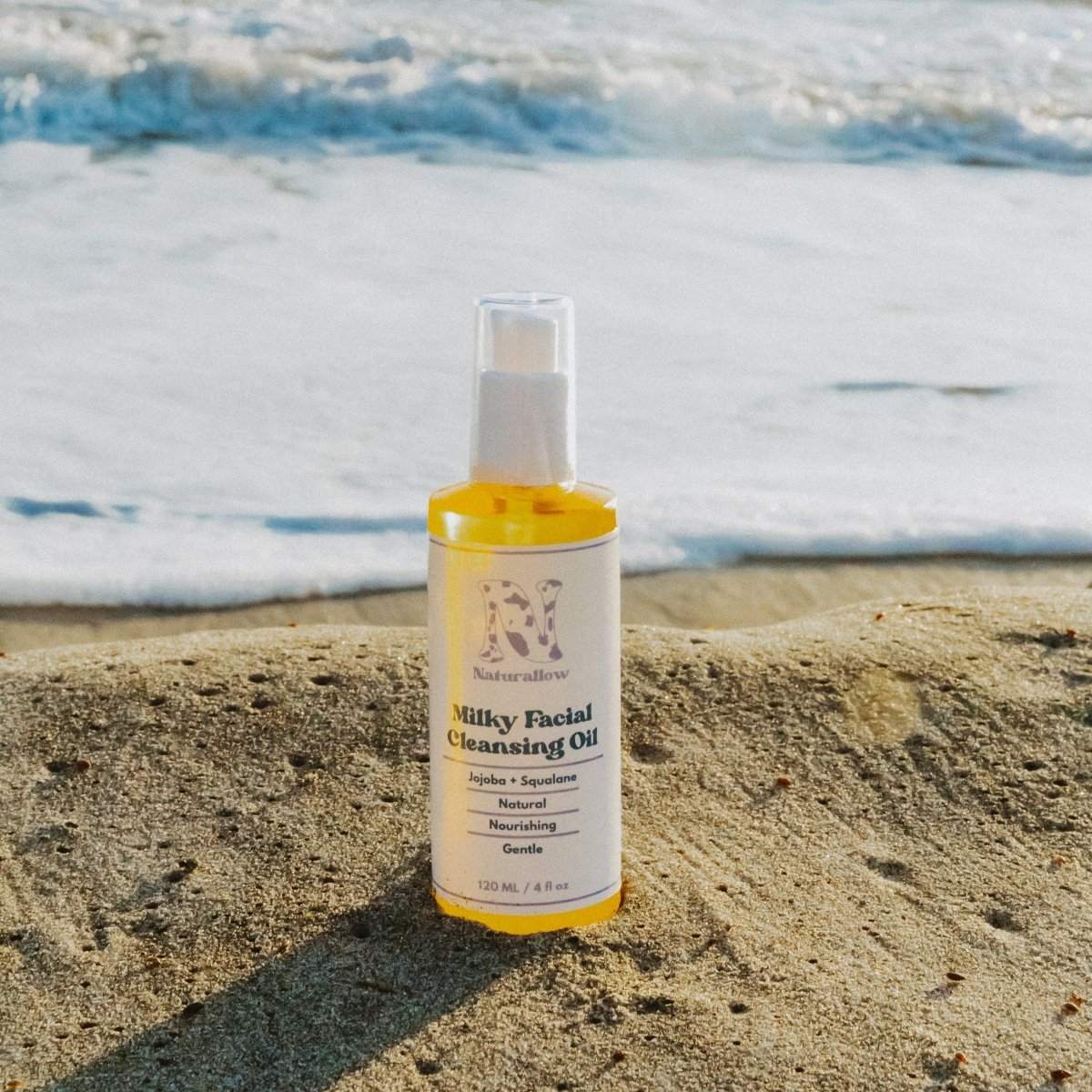 Naturallow Milky Facial Cleansing Oil, bottle on wet sand at the shoreline