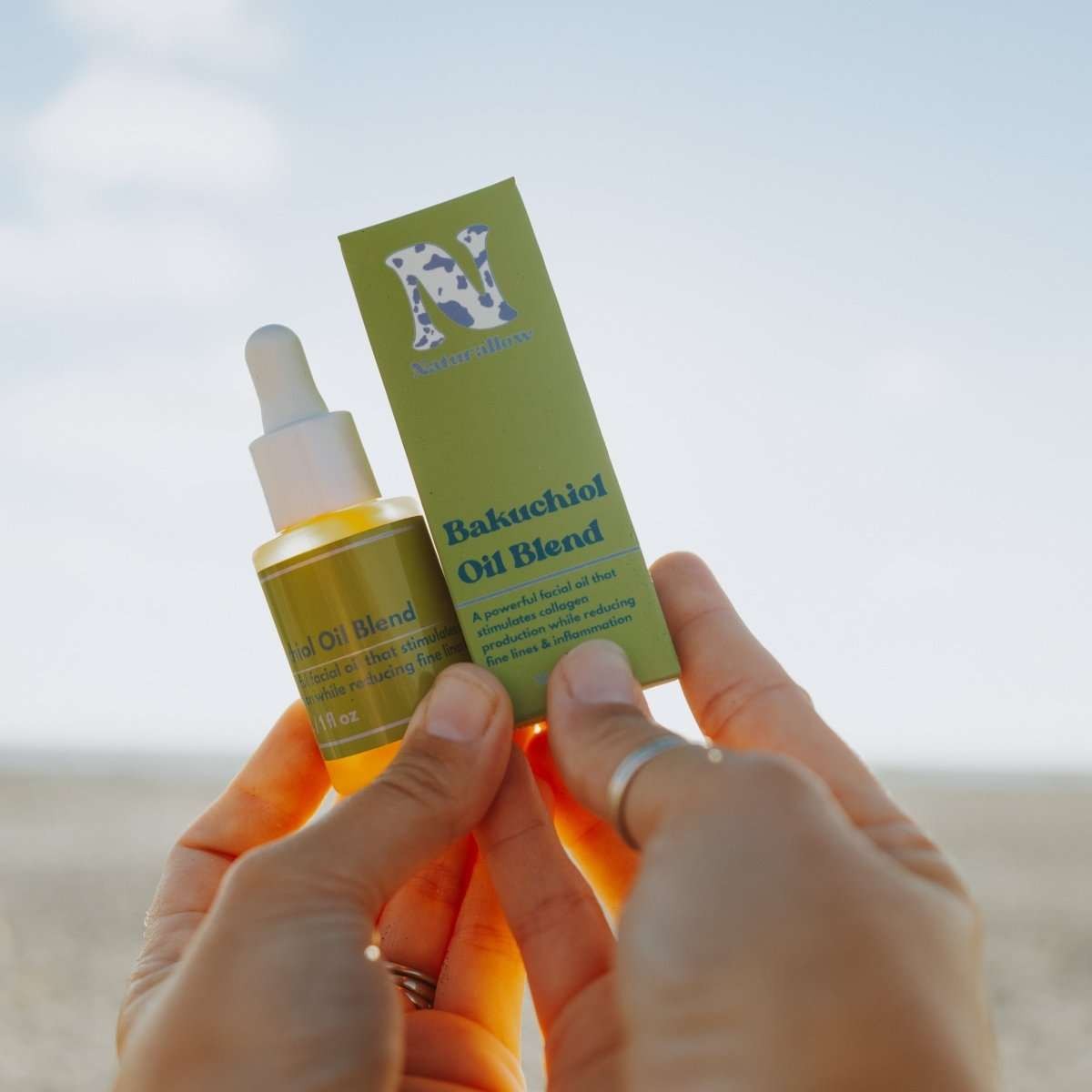 Naturallow Bakuchiol Facial Oil, hands holding the dropper bottle and box against the sky