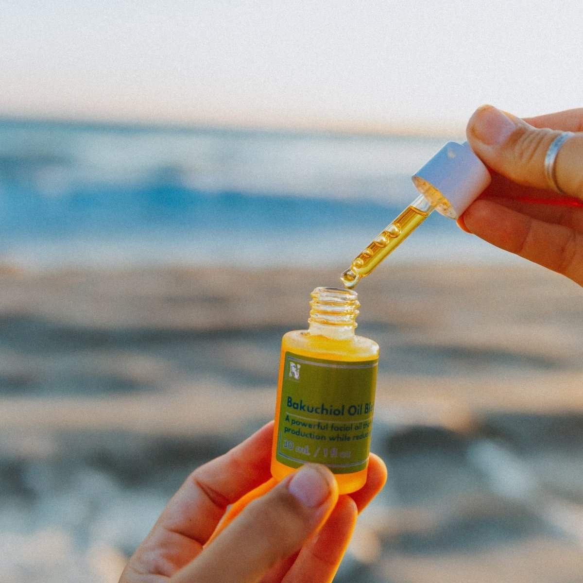Naturallow Bakuchiol Facial Oil, hand holding the open bottle and dropper by the ocean